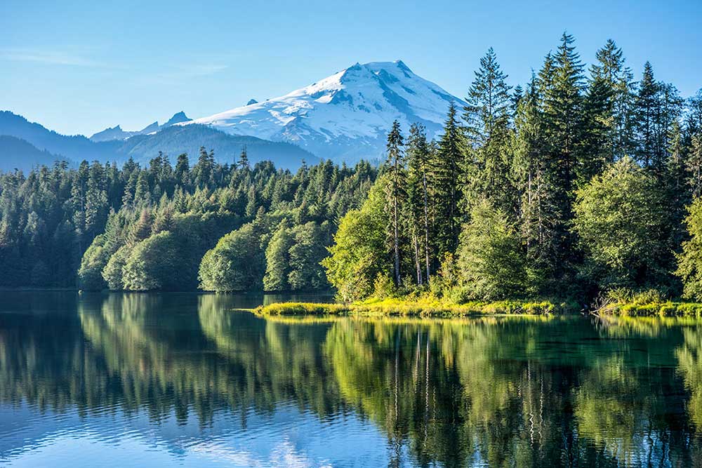 An image of a mountain lake, woodlands and Mt. Baker in the background